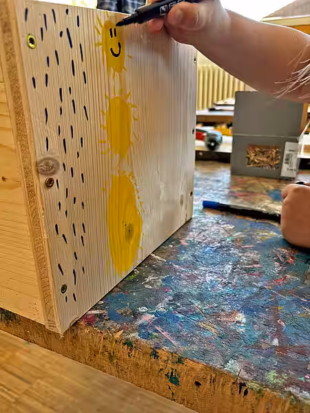 Kinderhände malen Sonnen auf das Holz des Igelhauses.