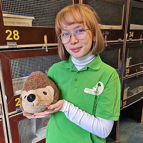 Angelina Pawel aus dem Igelzentrum Laatzen Eine Mitarbeiterin steht vor Igelboxen und hält einen Plüschigel