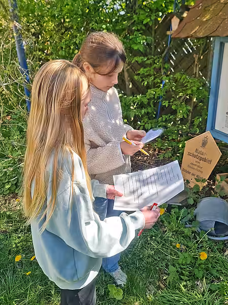 Zwei Mädchen lesen Quizfragen im Garten.